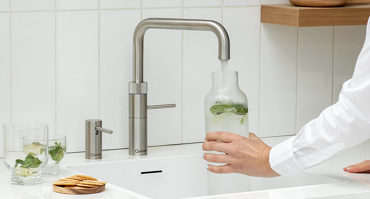 Person füllt Wasserkaraffe an moderner Küchenarmatur