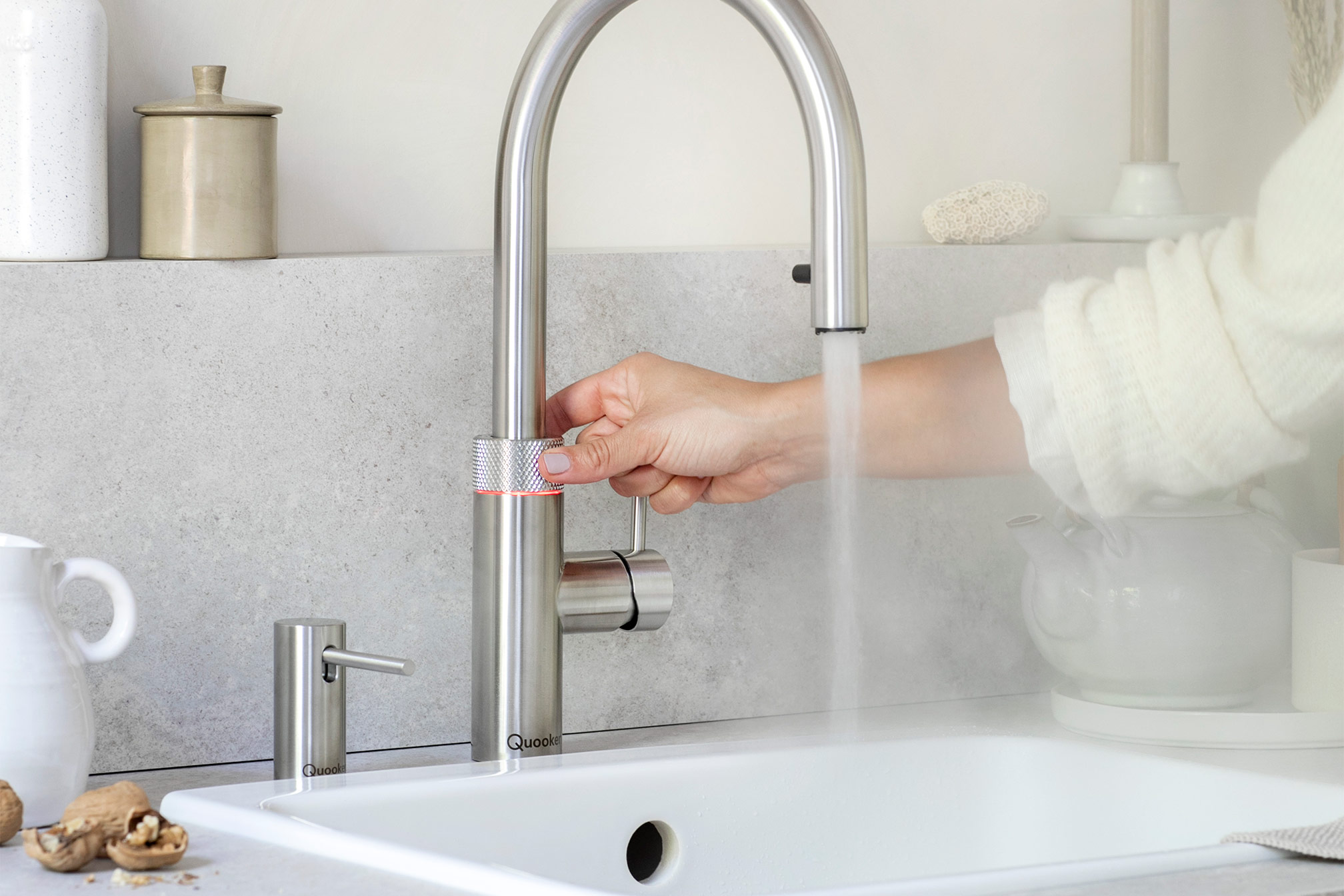 Quooker-Edelstahl Person öffnet Wasserhahn in moderner Kücheneinrichtung