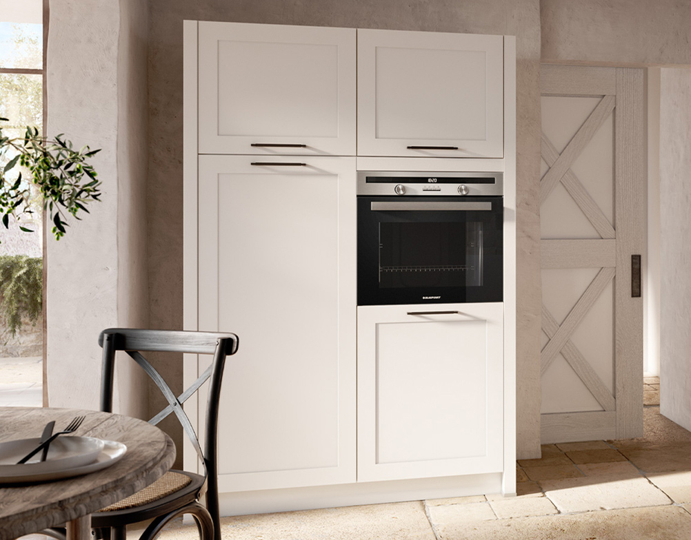 schrank-ravenna Weißer Einbauschrank im Landhausstil mit integriertem Backofen und schlichten Griffen, vor einer hellen Steinwand.